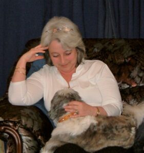 Lorraine Reed-Wenman wearing a white blouse and looking down at a dog on her lap