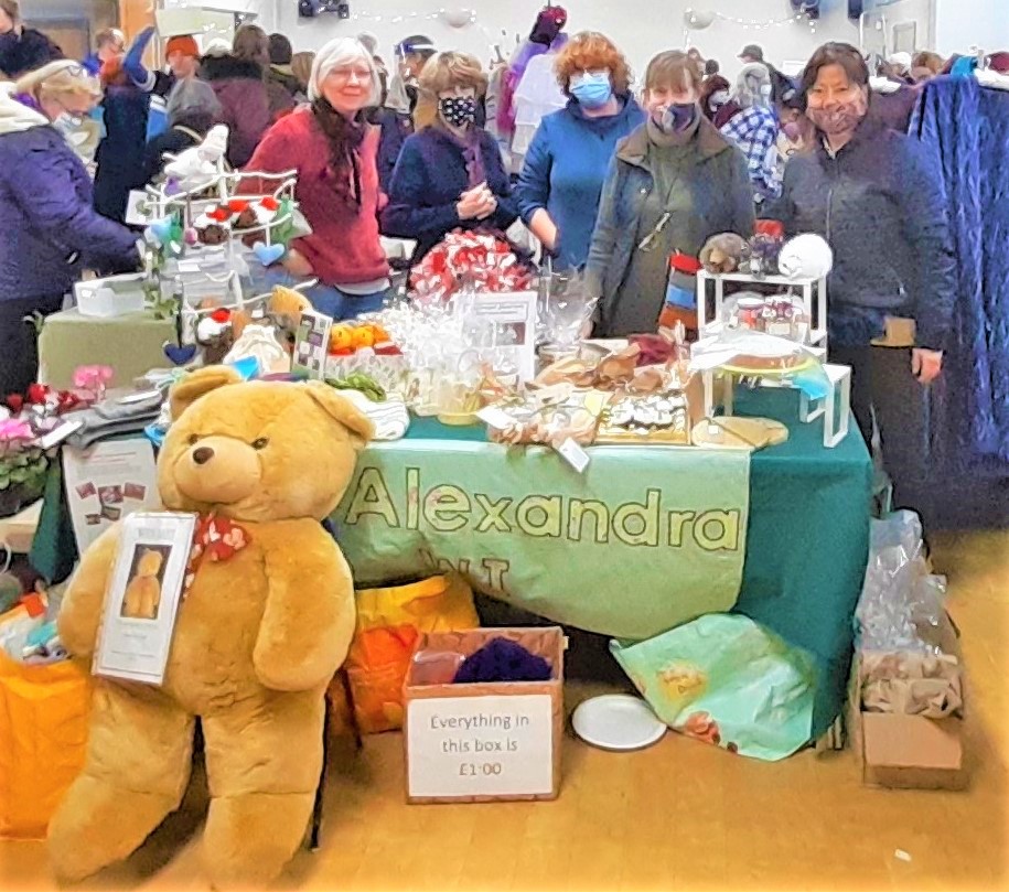 Five WI members standing behind the stall, with a giant light brown teddy bear on the floor in front
