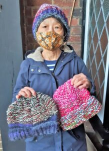 Woman holding two colourful knitted hats